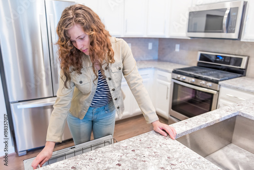Принти на полотні Young woman opening inspecting dishwasher in modern gray, brown kitchen features