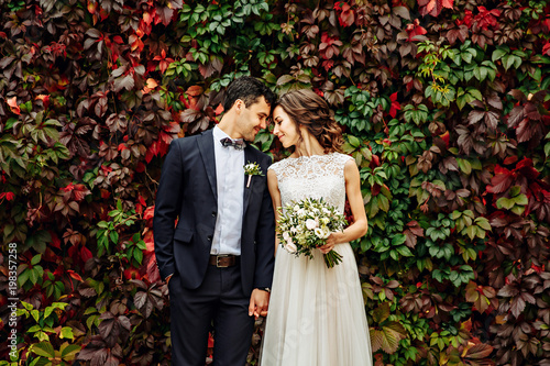 Print op canvas groom and bride posing in front ol old brick wall with ivy