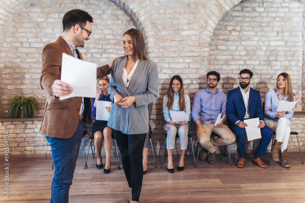 Fototapeta premium Businessman shaking hands with woman besides people waiting for job interview in a modern office