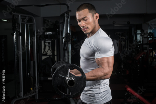 Muscular builder man training his body with barbell in Modern fitness center