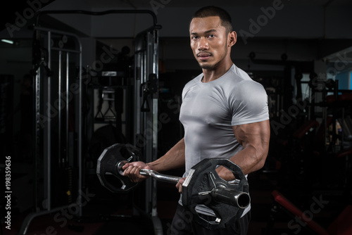 Muscular builder man training his body with barbell in Modern fitness center