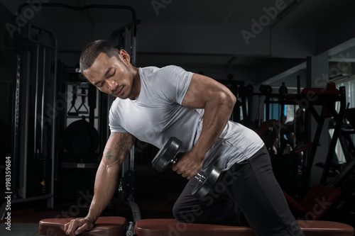 Muscular builder man training his body with dumbbell in Modern fitness center