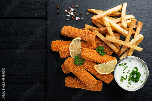 Fish fingers and fries with sauce on dark background. top view.