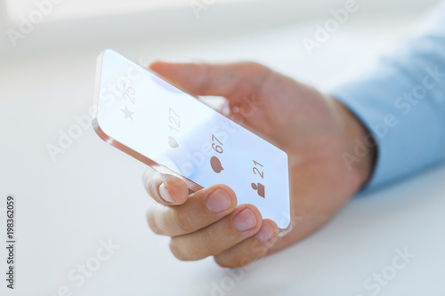 business, future technology and people concept - close up of male hand holding and showing transparent smartphone with social media icons over black background