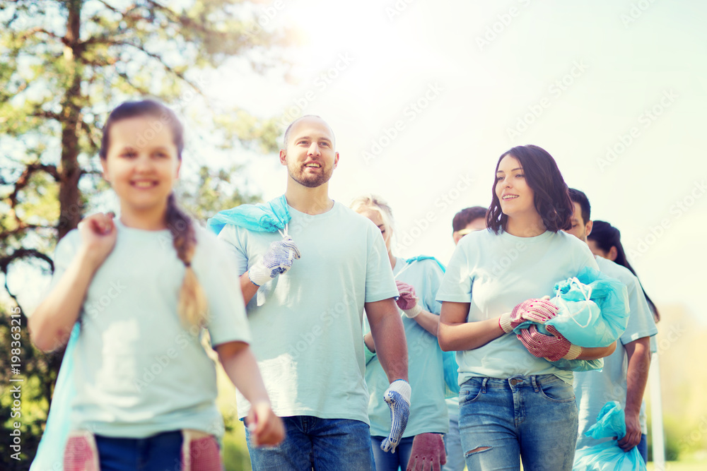 volunteering, charity, cleaning, people and ecology concept - group of happy volunteers with garbage bags walking in park volunteering, charity, cleaning, people and ecology concept - group of happy volunteers with garbage bags walking in park
