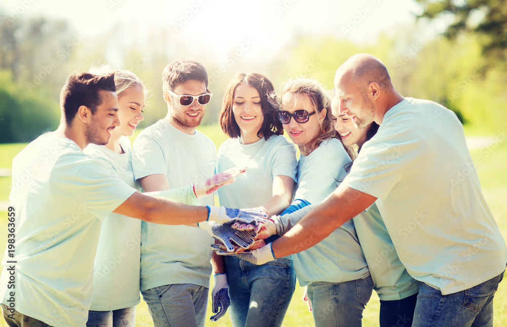 Obraz premium volunteering, charity, people, gesture and ecology concept - group of volunteers putting hands on top in park