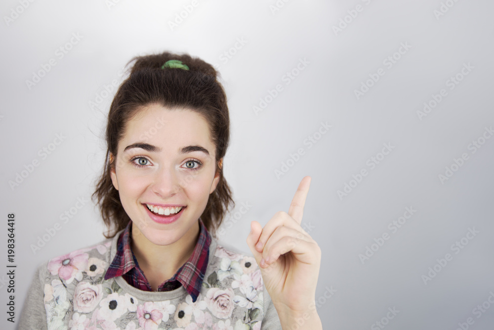 Smiling attractive young girl pointing away over gray background with copy space advertizing mock up Smiling attractive young girl pointing away over gray background with copy space advertizing mock up