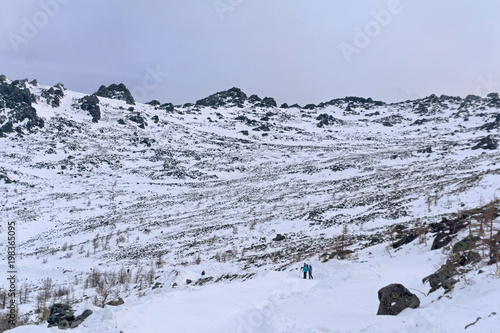 group of tourists away on a snow-covered mountain road crossing a rocky treeless slope..