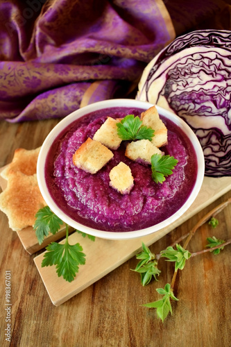 Cream soup made of red cabbage with croutons and parsley on wooden table