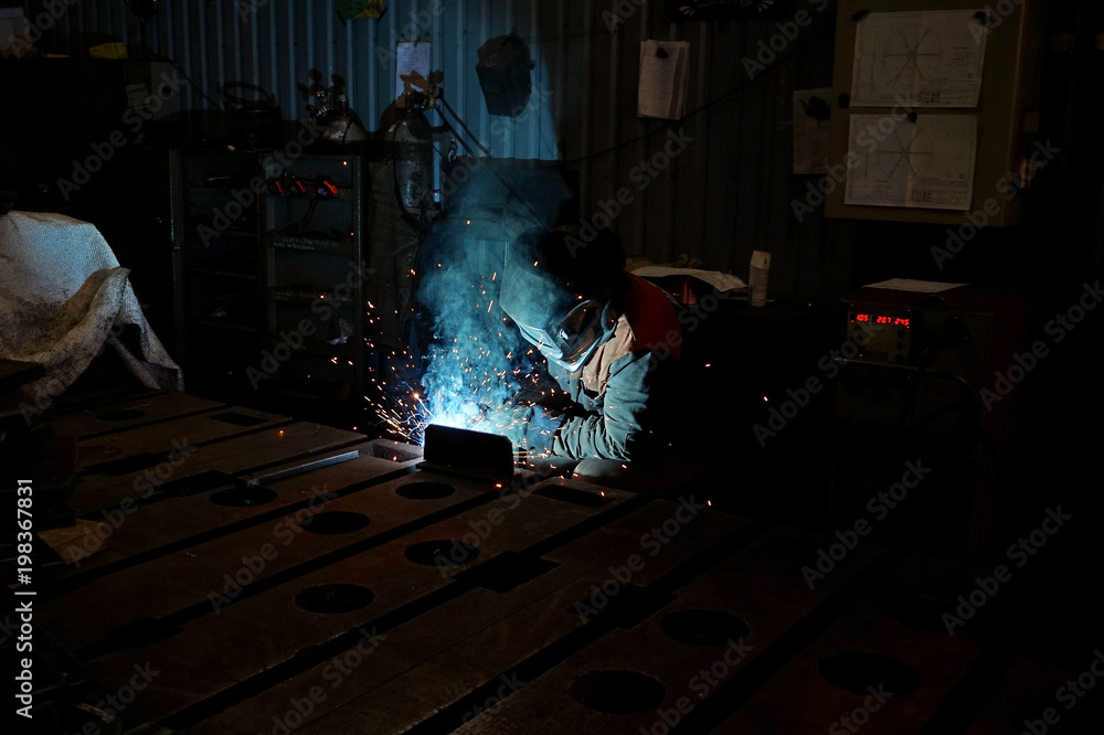 The welding welder is engaged in the manufacture of parts welding with sparks.