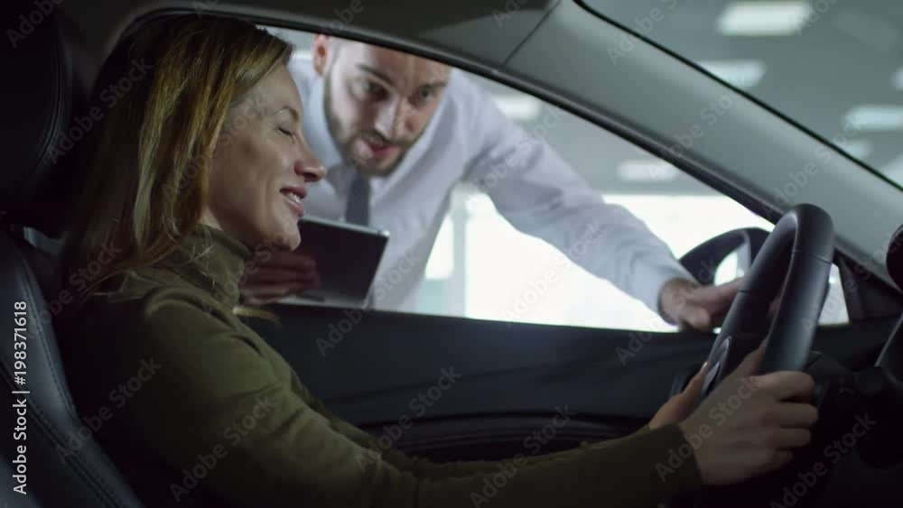 Tilt up of happy female client sitting in demo car and talking with cheerful professional auto salesman at dealership Tilt up of happy female client sitting in demo car and talking with cheerful professional auto salesman at dealership