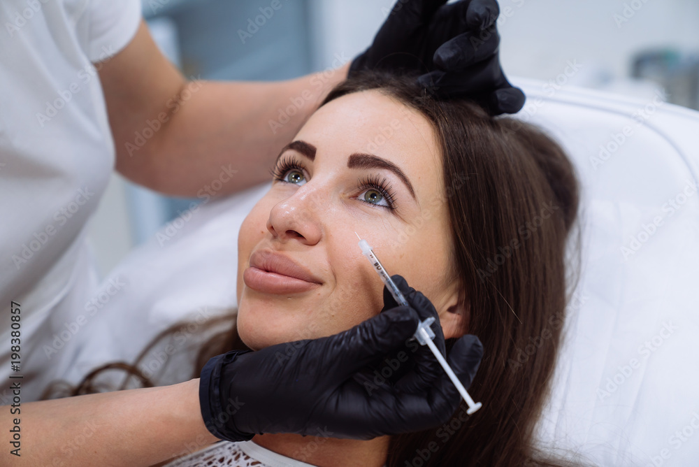 Close up beautiful female face and cosmetologist's hands with syringe during facial beauty injections. Rejuvenation and hydratation. Cosmetology concept