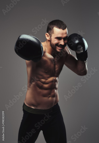A brutal shirtless caucasian sportsman in boxing gloves training isolated on a gray background.