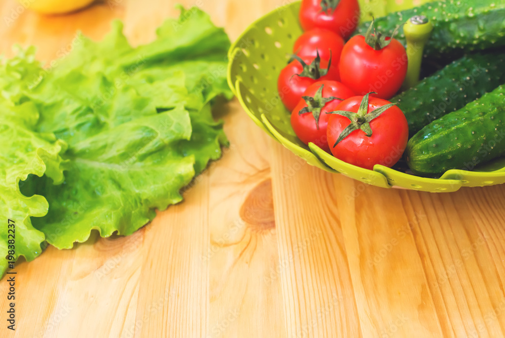 Fresh vegetables cucumbers and tomatoes in a green bowl on a wooden table next to green lettuce leaves. Vegetarian diet. Healthy diet and lifestyle Fresh vegetables cucumbers and tomatoes in a green bowl on a wooden table next to green lettuce leaves. Vegetarian diet. Healthy diet and lifestyle