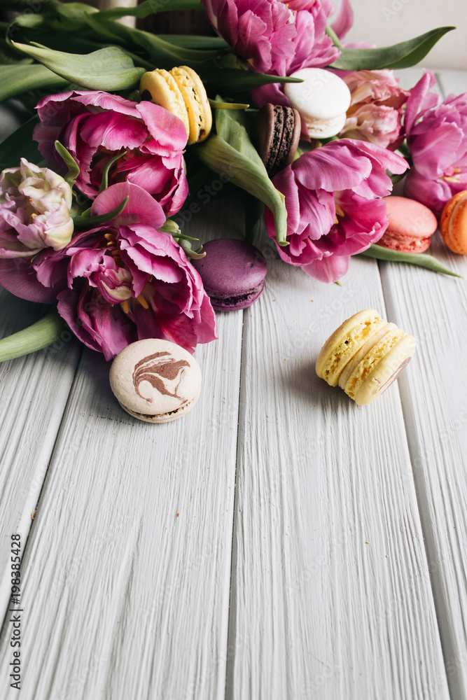 Delicious colorful macaroons and pink tulips on white wooden table, sweet dessert Delicious colorful macaroons and pink tulips on white wooden table, sweet dessert