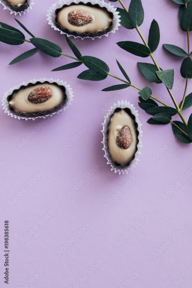Composition of delicious praline sweets with almonds on purple background