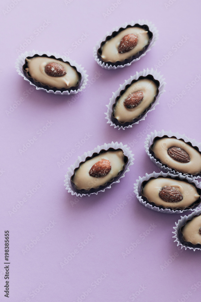 Composition of delicious praline sweets with almonds on purple background Composition of delicious praline sweets with almonds on purple background
