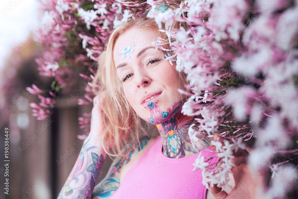 Fototapeta premium Tight portrait of blonde caucasian woman with tattoos near pink flowers
