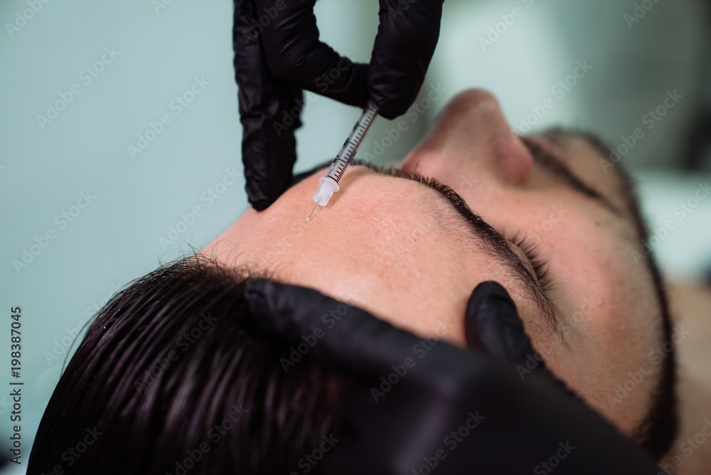Close up beautiful male face and cosmetologist's hands with syringe during facial beauty injections. Rejuvenation and hydratation. Cosmetology concept