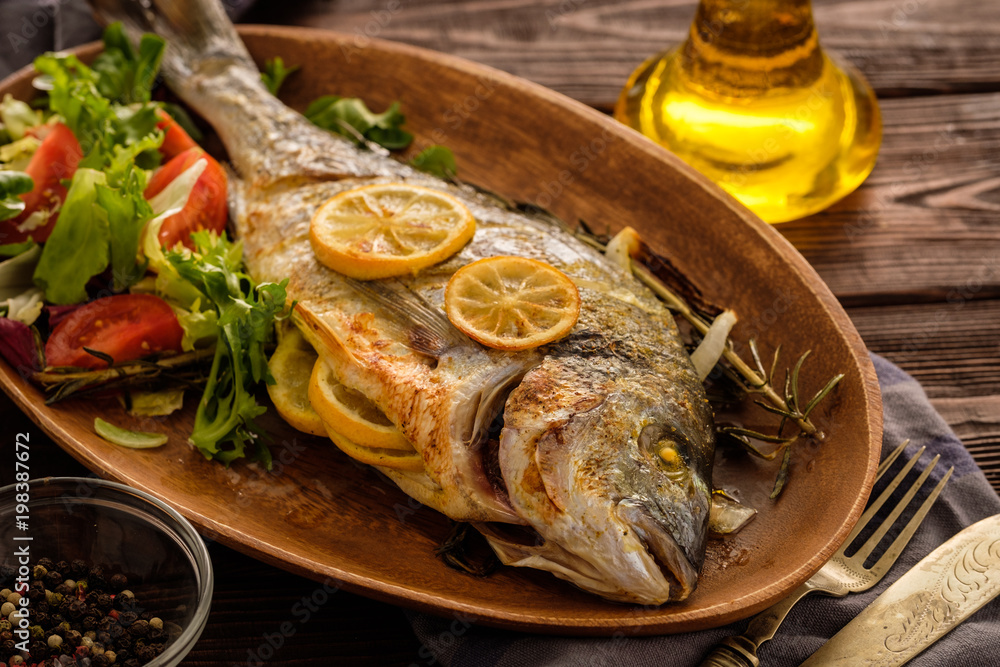 Grilled Dorado with lemon, thyme, rosemary and fresh salad on the wooden table. Grilled Dorado with lemon, thyme, rosemary and fresh salad on the wooden table.