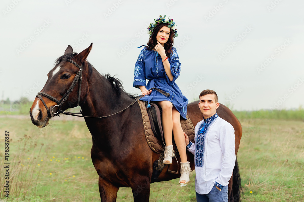 The girl elegantly sits on a horse and her boyfriend stands next to her and they look together in the camera lens The girl elegantly sits on a horse and her boyfriend stands next to her and they look together in the camera lens