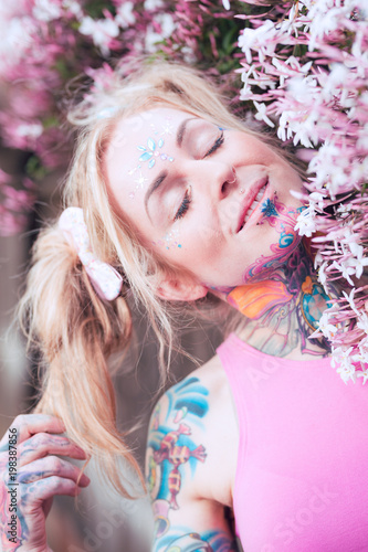 Tight portrait of blonde caucasian woman with tattoos near pink flowers