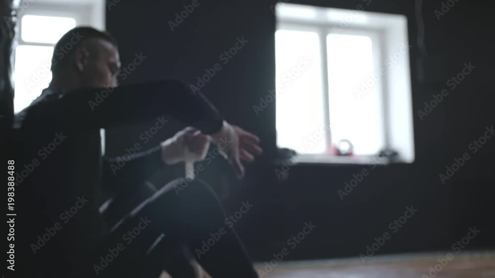 Side view of sportsman wrapping his hands with elastic bandage to protect them against injuries before doing boxing workout, medium shot Side view of sportsman wrapping his hands with elastic bandage to protect them against injuries before doing boxing workout, medium shot