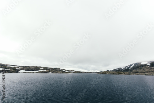 Typical norwegian landscape with snowy mountains and clear lake near the famous Trolltunga rock, Norway.