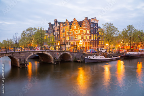 Amsterdam canal, bridge and typical houses, boats and bicycles during evening