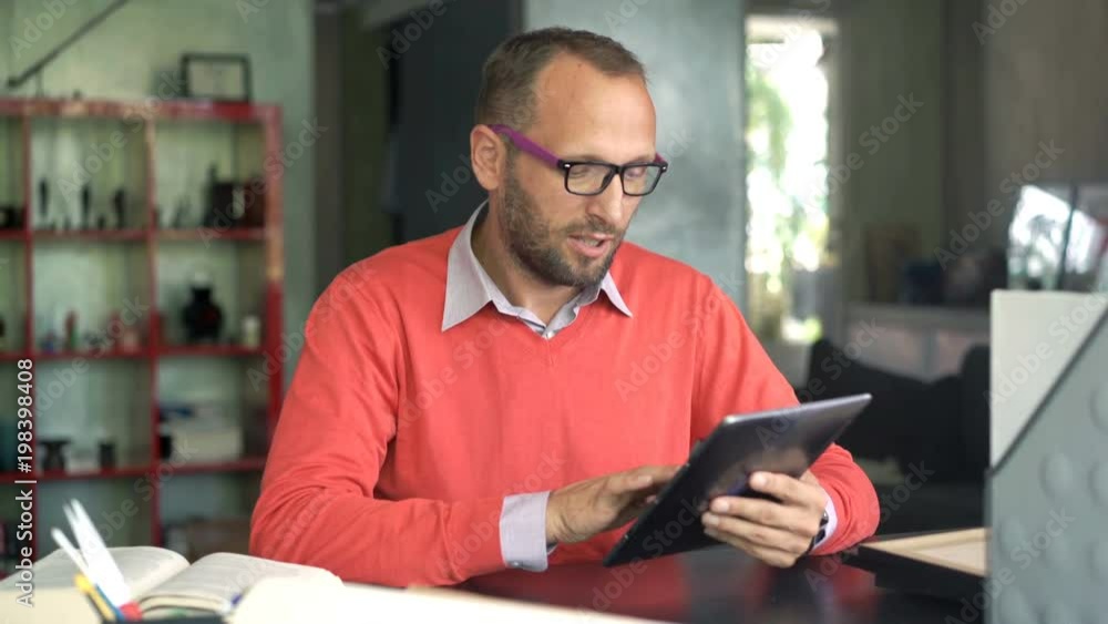 Young man with tablet talking to camera sitting by table at home
Young man with tablet talking to camera sitting by table at home
