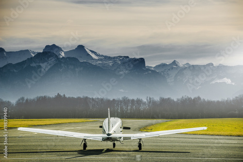 Propeller plane parking at the airport. Small airfield in front of high mountains. Sunset over mountains.