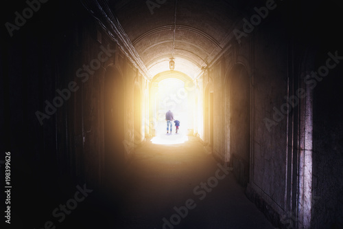 Silhouettes of man and child, father and daughter, walking into light from dark tunnel
