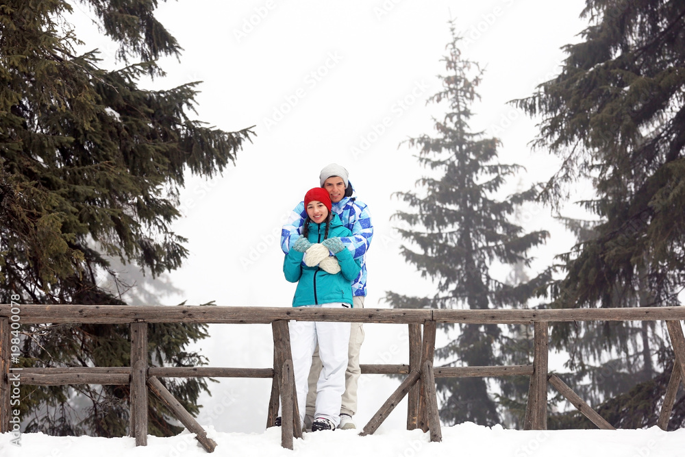 Lovely couple standing on bridge in snowy forest. Winter vacation