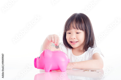 Little asian girl putting coin into pink piggy bank over white background