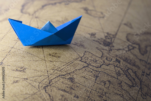 Blue paper ship isolated on old map background. Paper craft and origami. Paper ship on world map