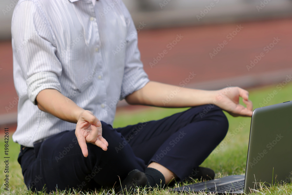 Cropped image of relaxed young Asian business man with laptop doing yoga position on the green grass.