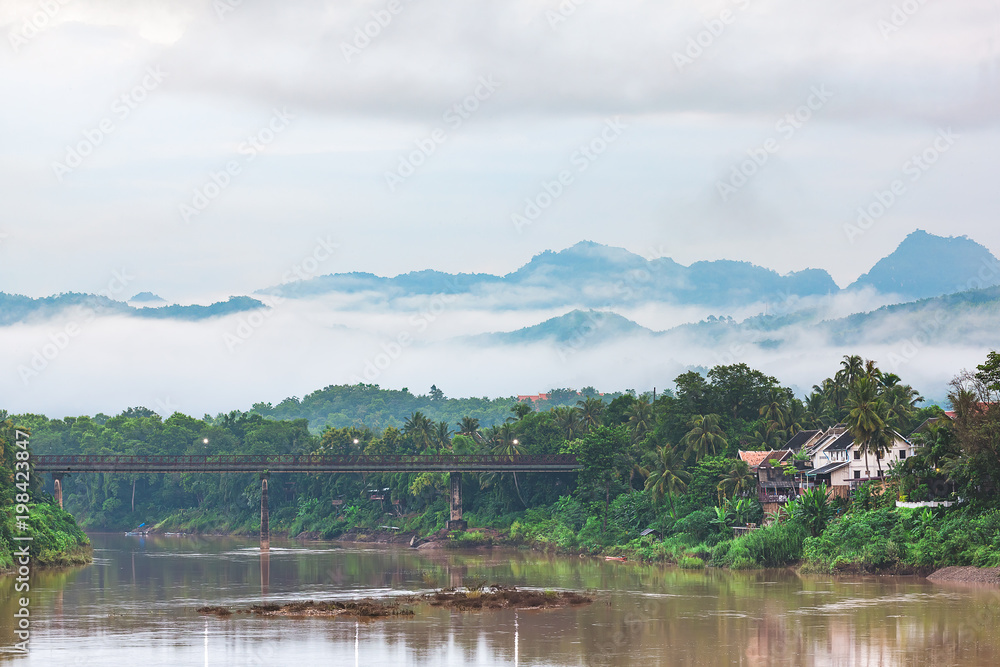 Nam Khan (Khan River) and Old Bridge Beautiful landscape in Luang Prabang. Behind the mountains and morning mist. Nam Khan (Khan River) and Old Bridge Beautiful landscape in Luang Prabang. Behind the mountains and morning mist.