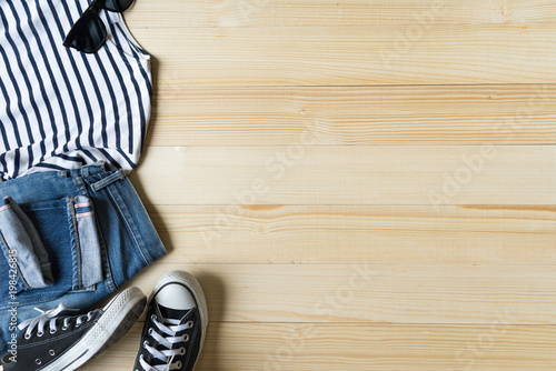 Top view of casual clothes, stripes t-shirt, jeans, sneaker and sun glasses on wooden background with copy space
