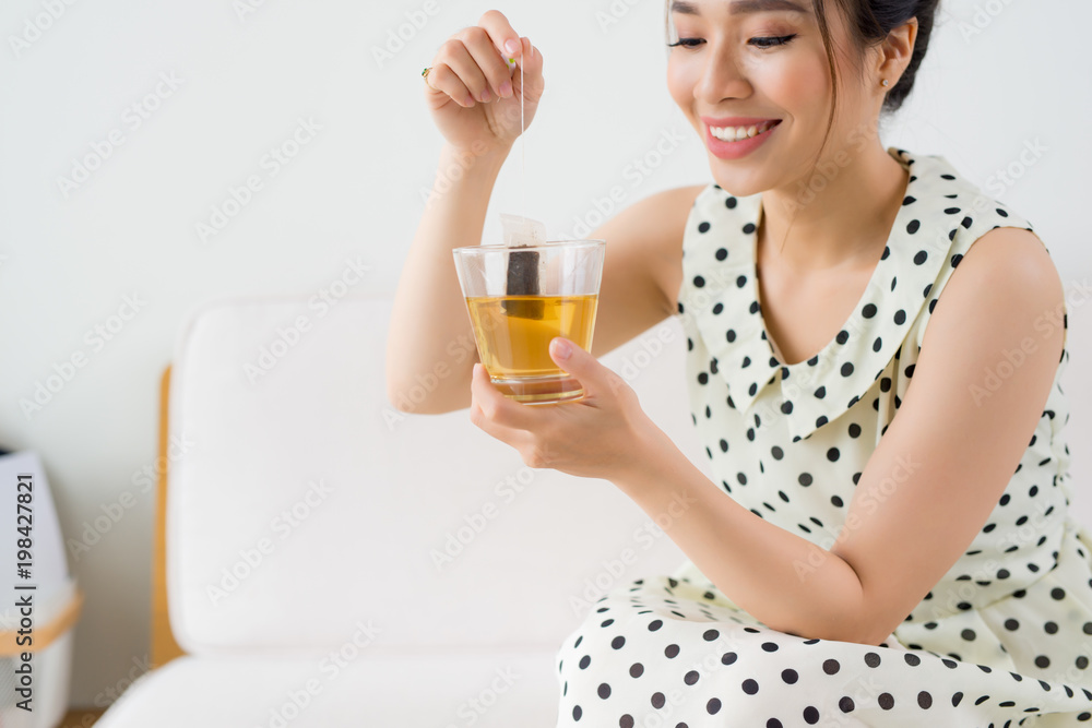 Young asian woman sitting on couch at home and drinking tea Young asian woman sitting on couch at home and drinking tea