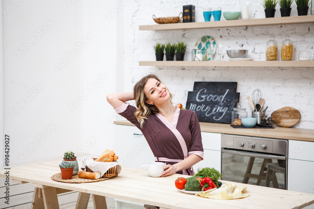 A beautiful girl sips awakens at breakfast in the kitchen. Cheerful girl in the dining room at lunch. Lifestyle. Space for text.
