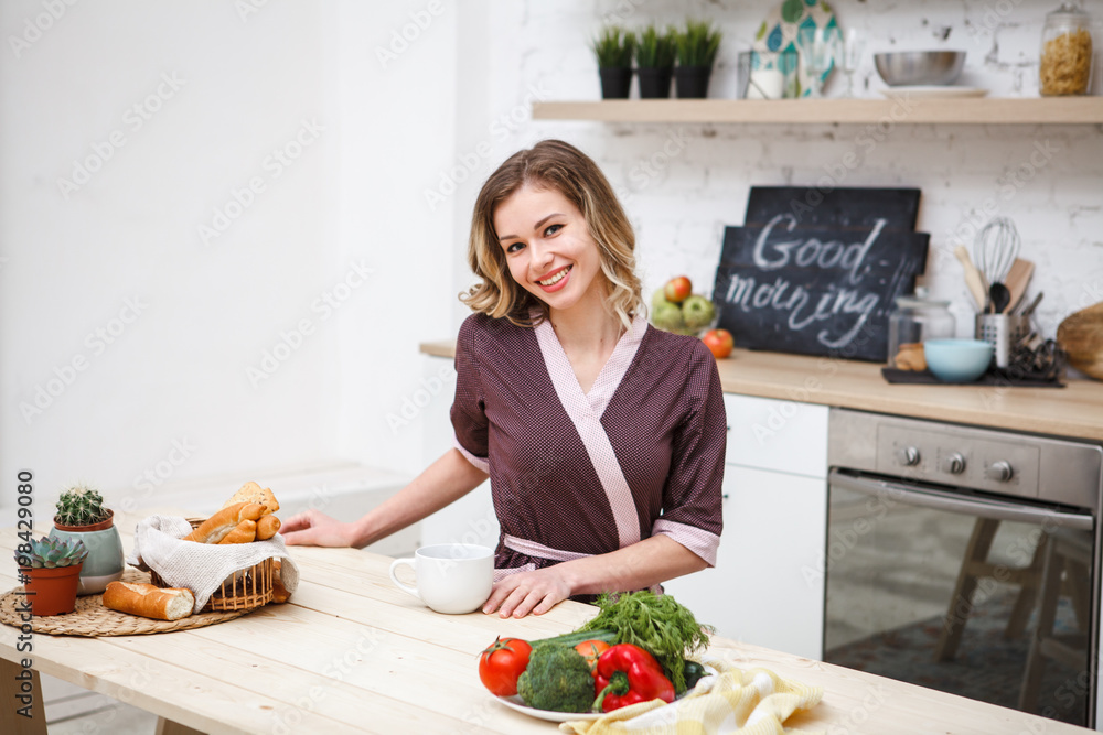 Cheerful girl in the kitchen at lunch. Portrait of a beautiful girl at home in the dining room at breakfast, who looks at the camera and smiles. Space for text.