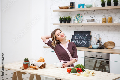 A beautiful girl sips awakens at breakfast in the kitchen. Cheerful girl in the dining room at lunch. Lifestyle. Space for text.