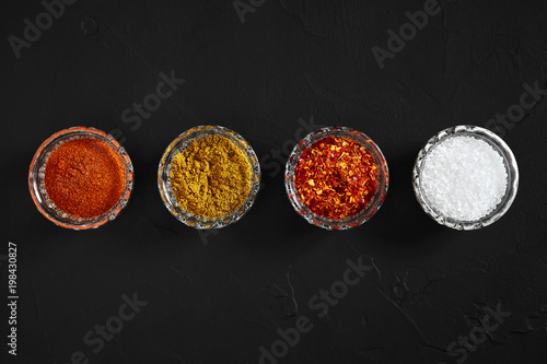 Cooking using fresh ground spices with four small bowls of spice on a black table overhead view with copyspace