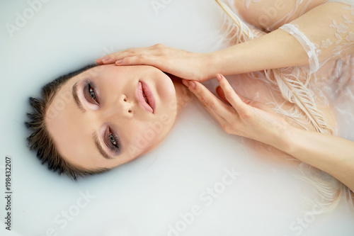 Bright Studio.Delicate and sensual atmosphere of peace and tranquility. Relaxation.Portrait of a beautiful girl with plump lips, graceful thin wrists, wet hair. Lying in the milk, top view.