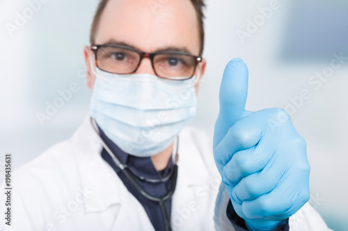 Ein Arzt mit Mundschutz und blauen Latexhandschuhen zeigt Daumen hoch