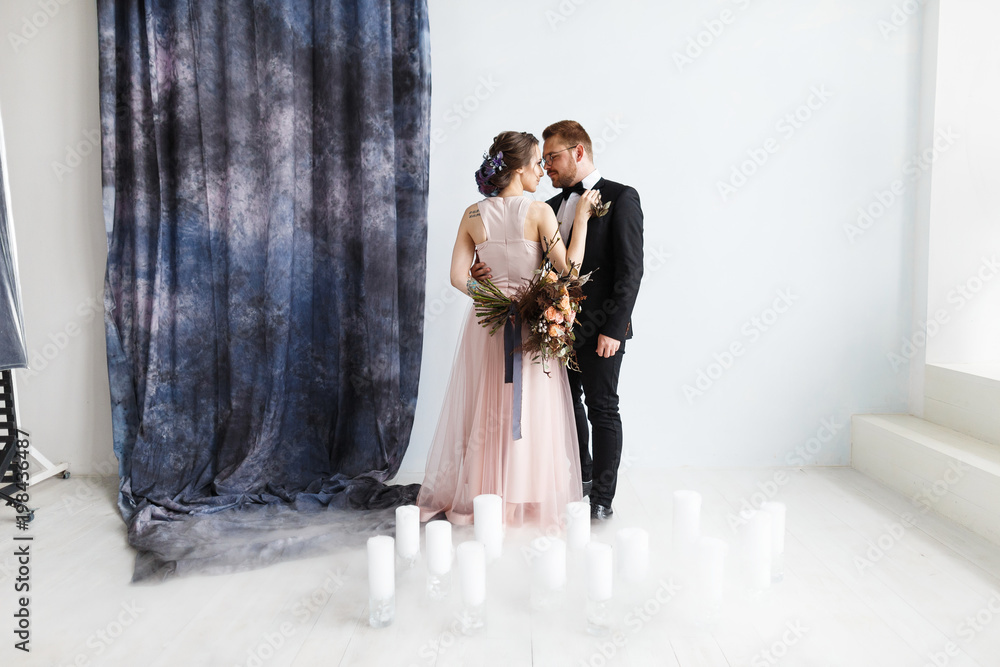 Full-length portrait of pretty newlyweds with bouquet. isolated white background and blue curtain. Studio horizontal shot with dry ice smoke