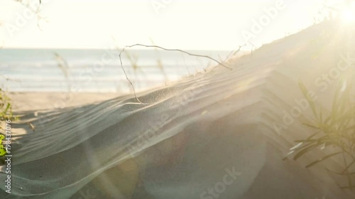 Slow motion of sand blowing off the beach at sunrise from a large dune