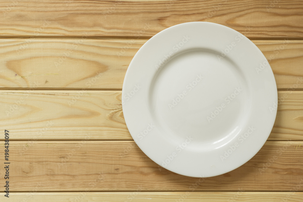 White empty plate at the wooden table with copy space. White empty plate at the wooden table with copy space.