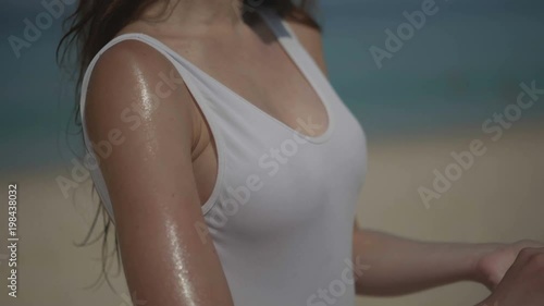 Beautiful girl in swimsuit applying sunscreen lotion tan oil on body at the tropical beach during summer holiday - video in slow motion