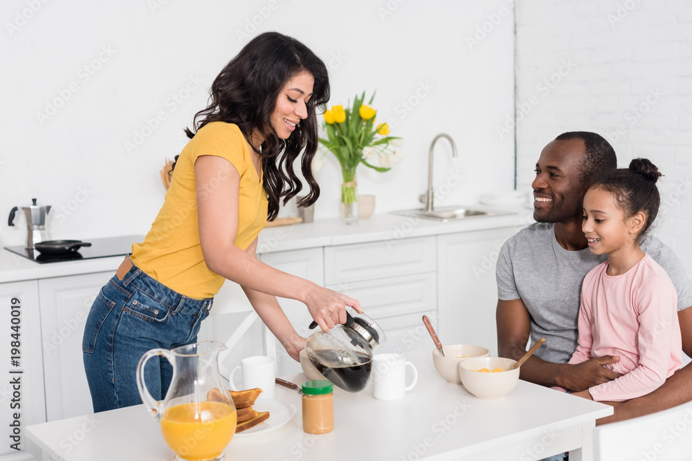 woman pouring coffee into cups for husband and daughter woman pouring coffee into cups for husband and daughter